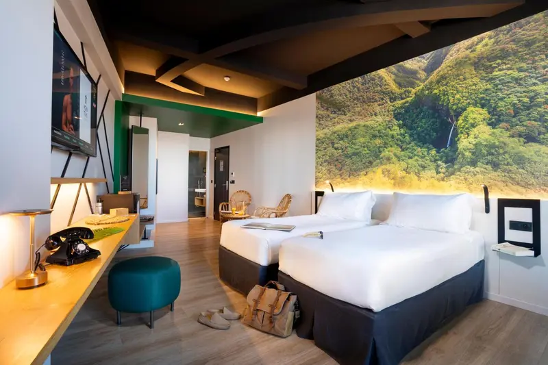 Une chambre lumineuse avec deux lits simples et un mur décoré d'un paysage tropical.