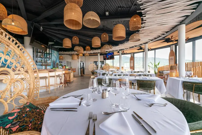 Une salle lumineuse avec des tables dressées et des suspensions en rotin.