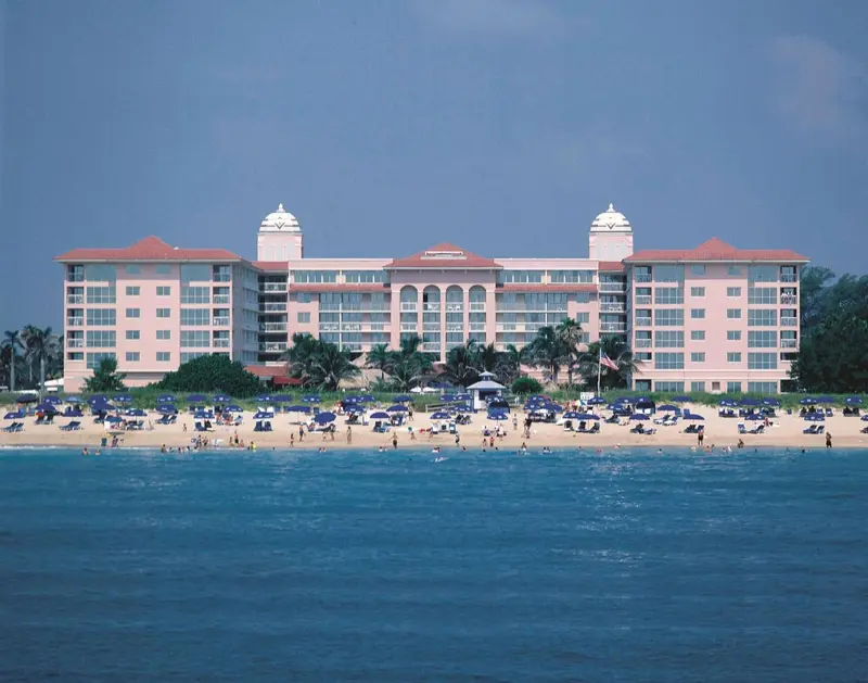 Vue d'un bâtiment rose et blanc avec des transats bleus sur une plage ensoleillée.