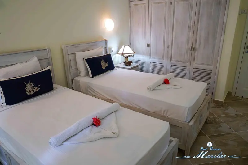 Une chambre lumineuse avec deux lits simples décorés de fleurs et de serviettes enroulées.
