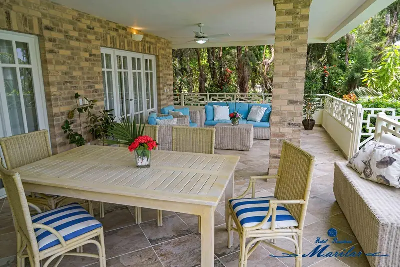 Une table et des chaises en osier sont disposées sur une terrasse carrelée ombragée.
