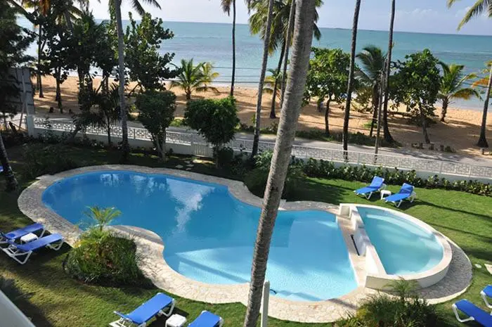 Piscine turquoise bordée de transats dans un jardin tropical face à la mer.