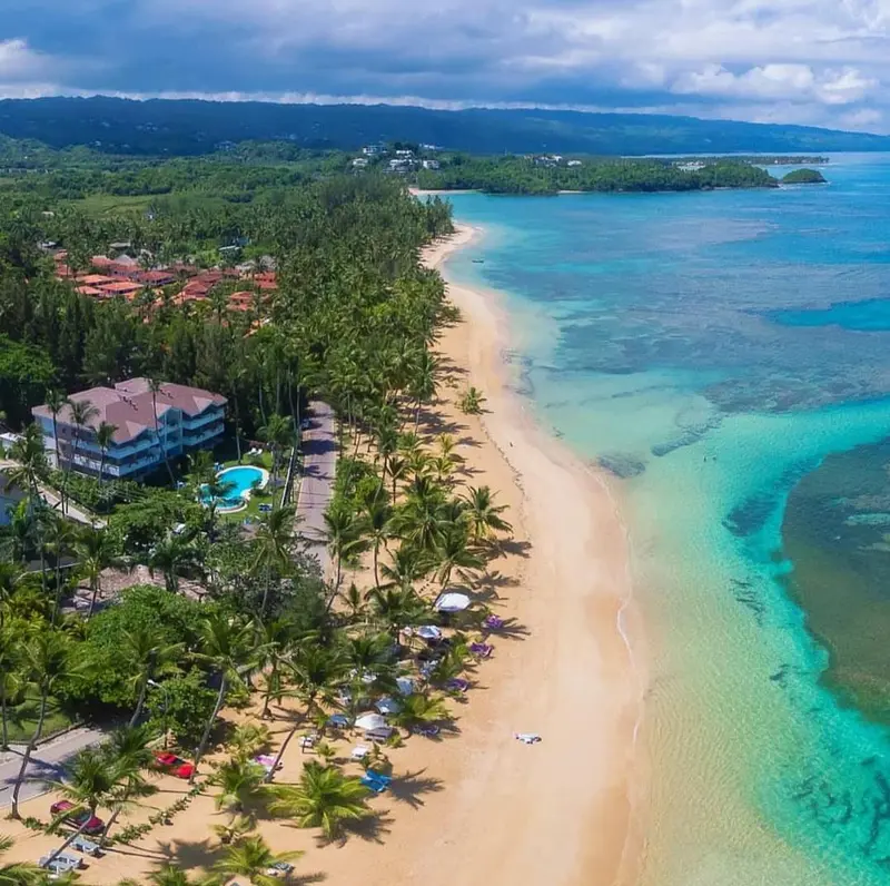 Vue aérienne d'une plage de sable fin bordée de palmiers et d'une eau turquoise.