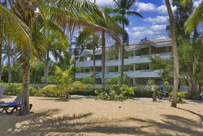 Bâtiment blanc à balcons donnant sur une plage de sable fin bordée de palmiers.