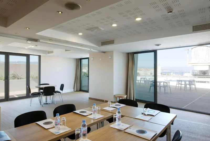 Une salle lumineuse avec des tables et des chaises, donnant sur une terrasse et une vue sur la mer.