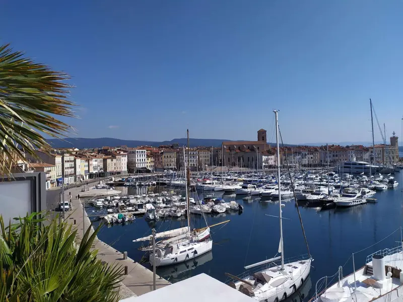 Vue d'un port de plaisance ensoleillé avec des bateaux amarrés et une ville en arrière-plan.