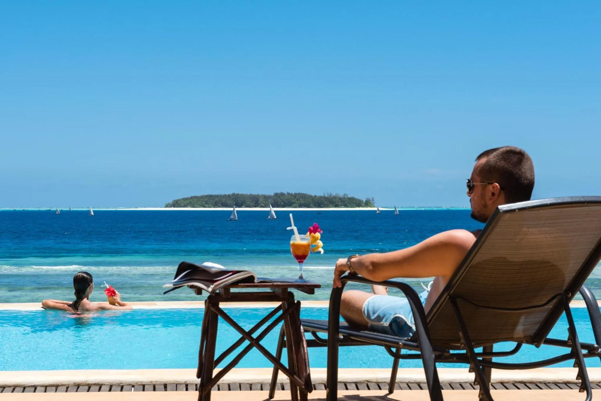 Un homme se détend sur un transat au bord d'une piscine turquoise.