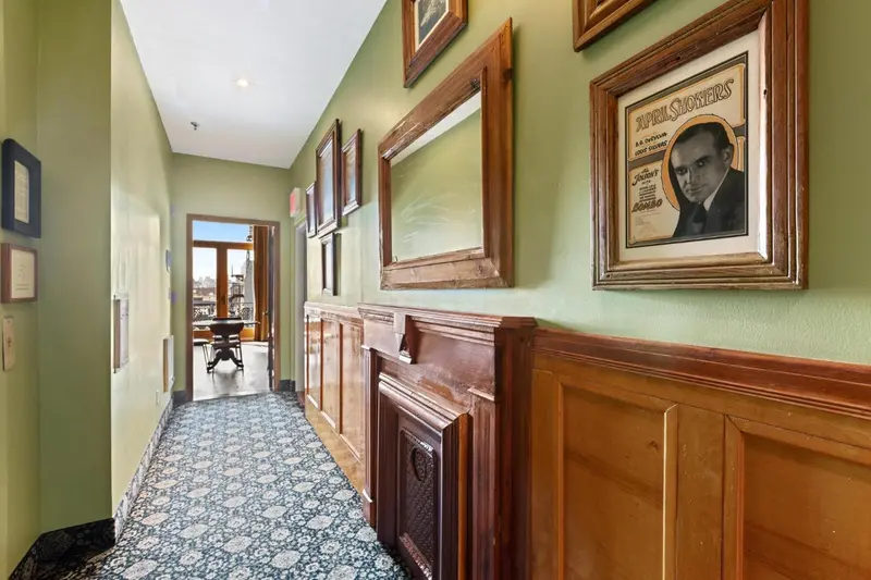Un couloir décoré de boiseries et de tableaux mène vers une pièce lumineuse.