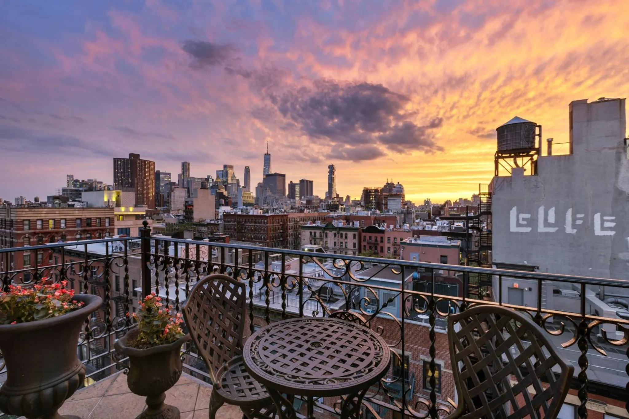 Terrasse avec mobilier de jardin et vue sur une ville au coucher du soleil.