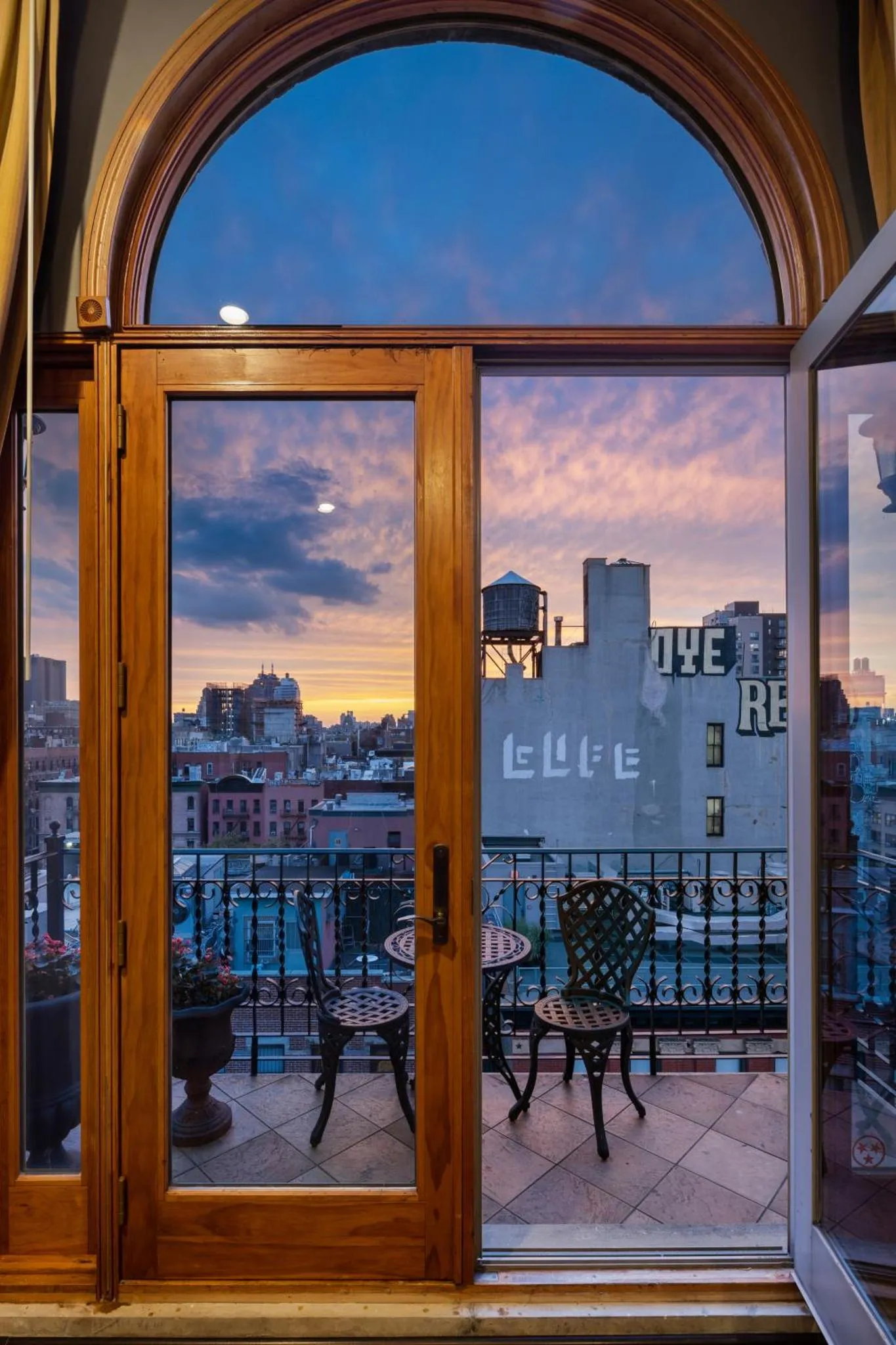 Vue sur une ville au crépuscule depuis un balcon avec des meubles en fer forgé.