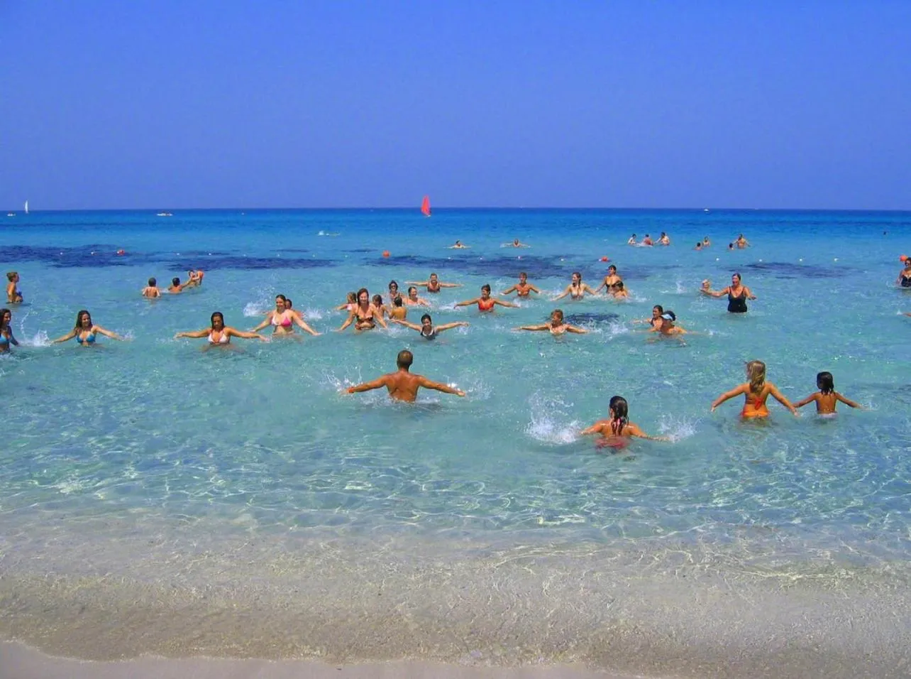 Groupe de personnes dans une eau turquoise peu profonde sur une plage ensoleillée.