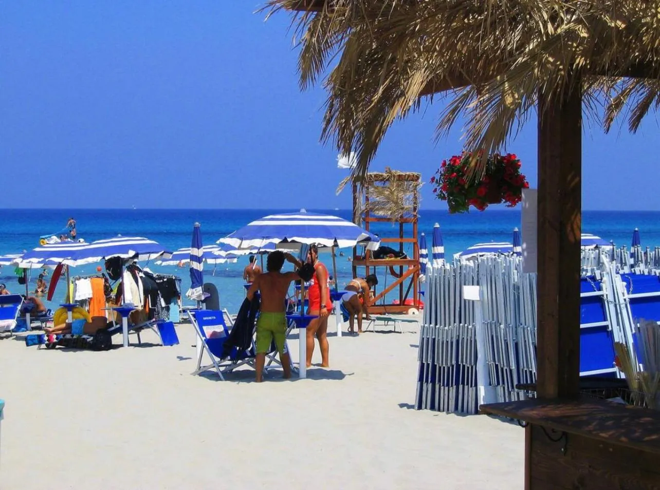 Plage ensoleillée avec parasols et transats face à la mer turquoise.