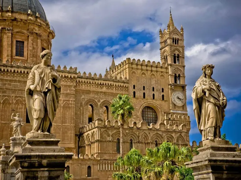 Façade d'une cathédrale ornée de statues et de palmiers sous un ciel bleu.