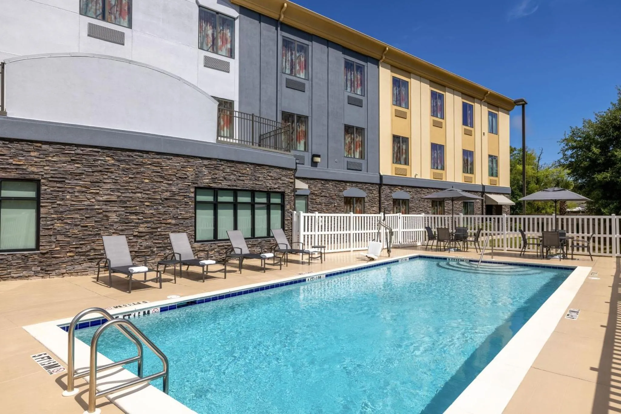 Une piscine rectangulaire avec des transats et des parasols à proximité d'un bâtiment.