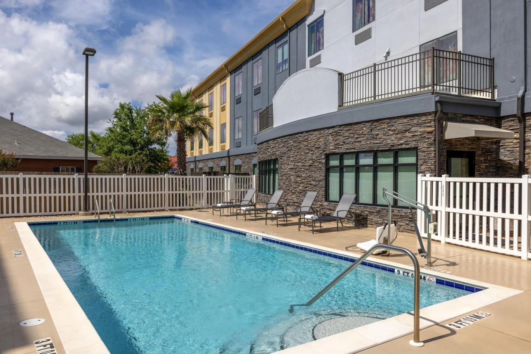 Une piscine rectangulaire avec des chaises longues est devant un bâtiment à plusieurs étages.