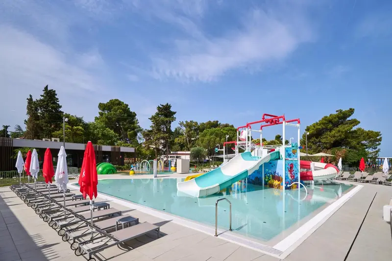Une piscine avec toboggans et transats sous des parasols.