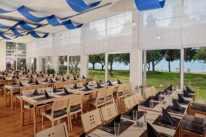 Une salle lumineuse avec des tables dressées pour un repas face à une vue sur la mer.