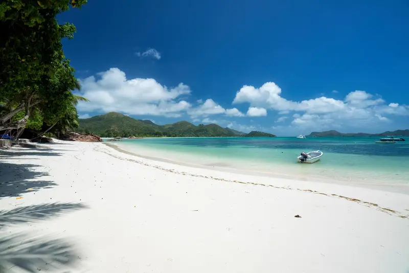 Plage de sable blanc bordée d'une eau turquoise sous un ciel bleu nuageux.