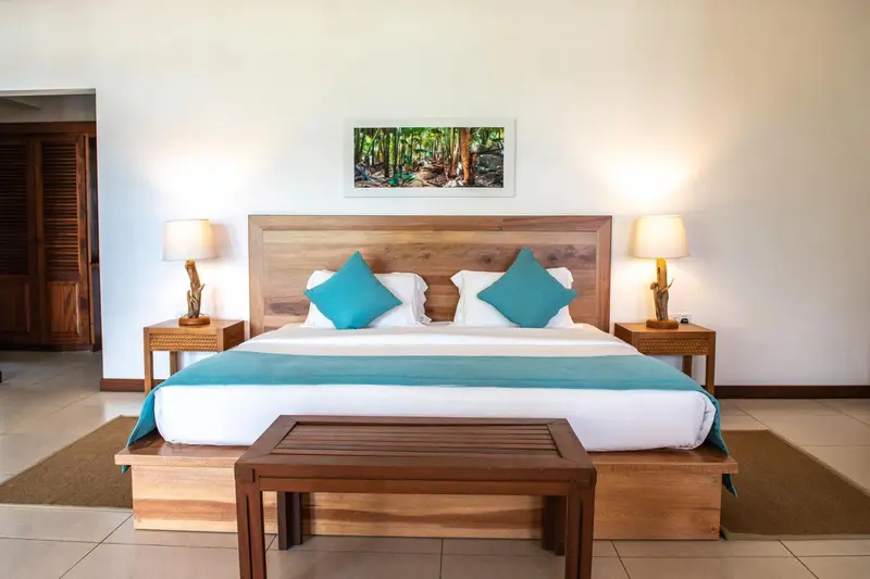 Une chambre lumineuse avec un grand lit recouvert d'une courtepointe turquoise et de coussins assortis.