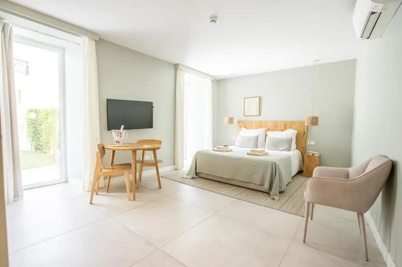 Chambre lumineuse avec un lit fait et un coin repas près d'une baie vitrée.