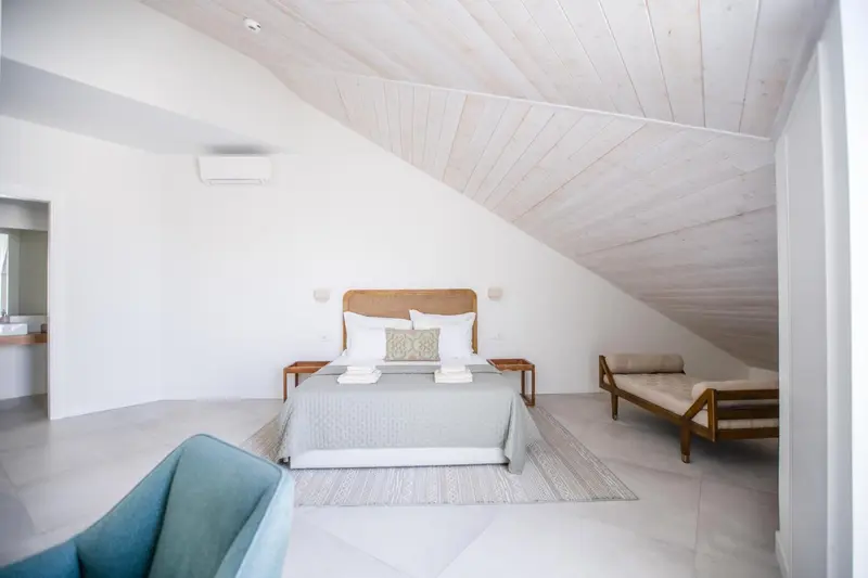 Une chambre lumineuse aux murs blancs et au plafond en pente.