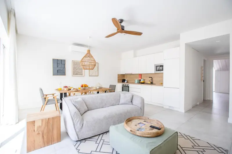 Interieur lumineux avec canape gris, table a manger et cuisine blanche.