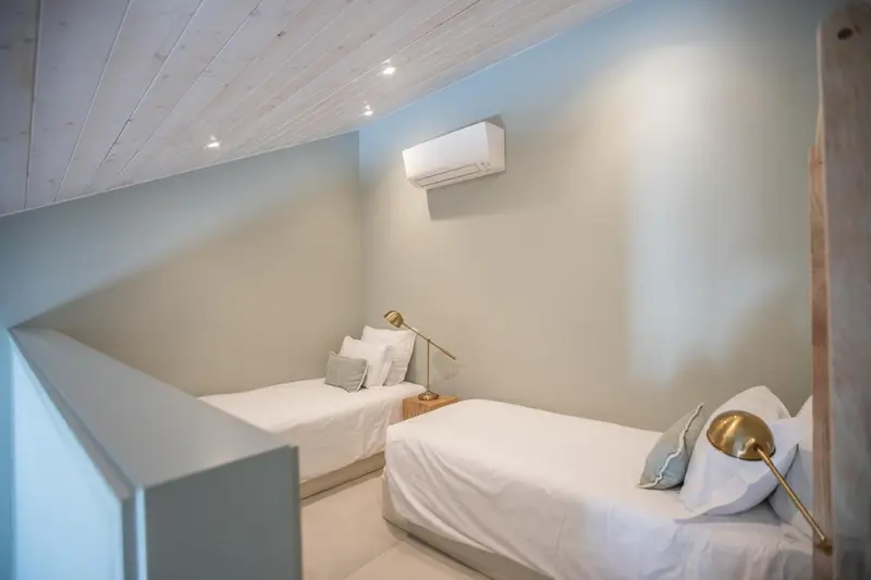 Une chambre lumineuse avec deux lits simples et une climatisation murale.