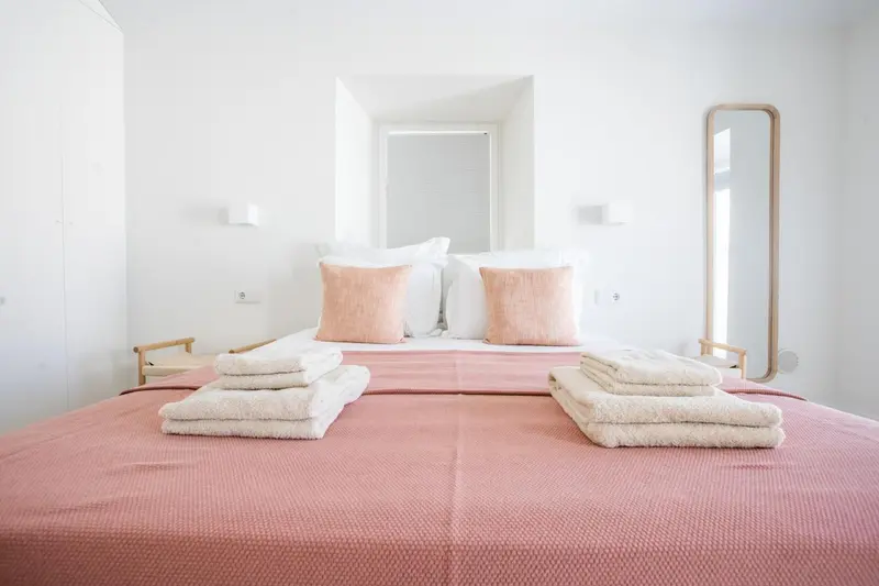 Une chambre lumineuse avec un grand lit recouvert d'une couverture rose et de coussins.