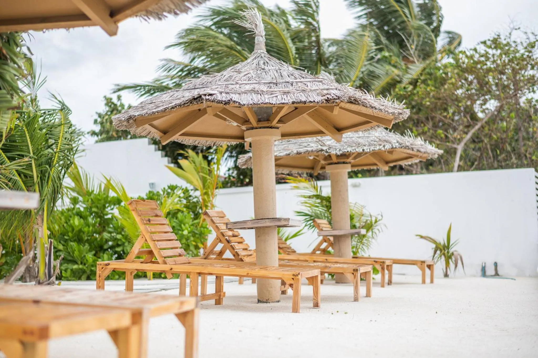 Transats en bois sous des parasols de chaume sur une plage de sable blanc.