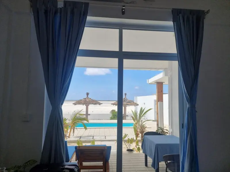 Vue sur une piscine et la mer depuis une ouverture avec rideaux.