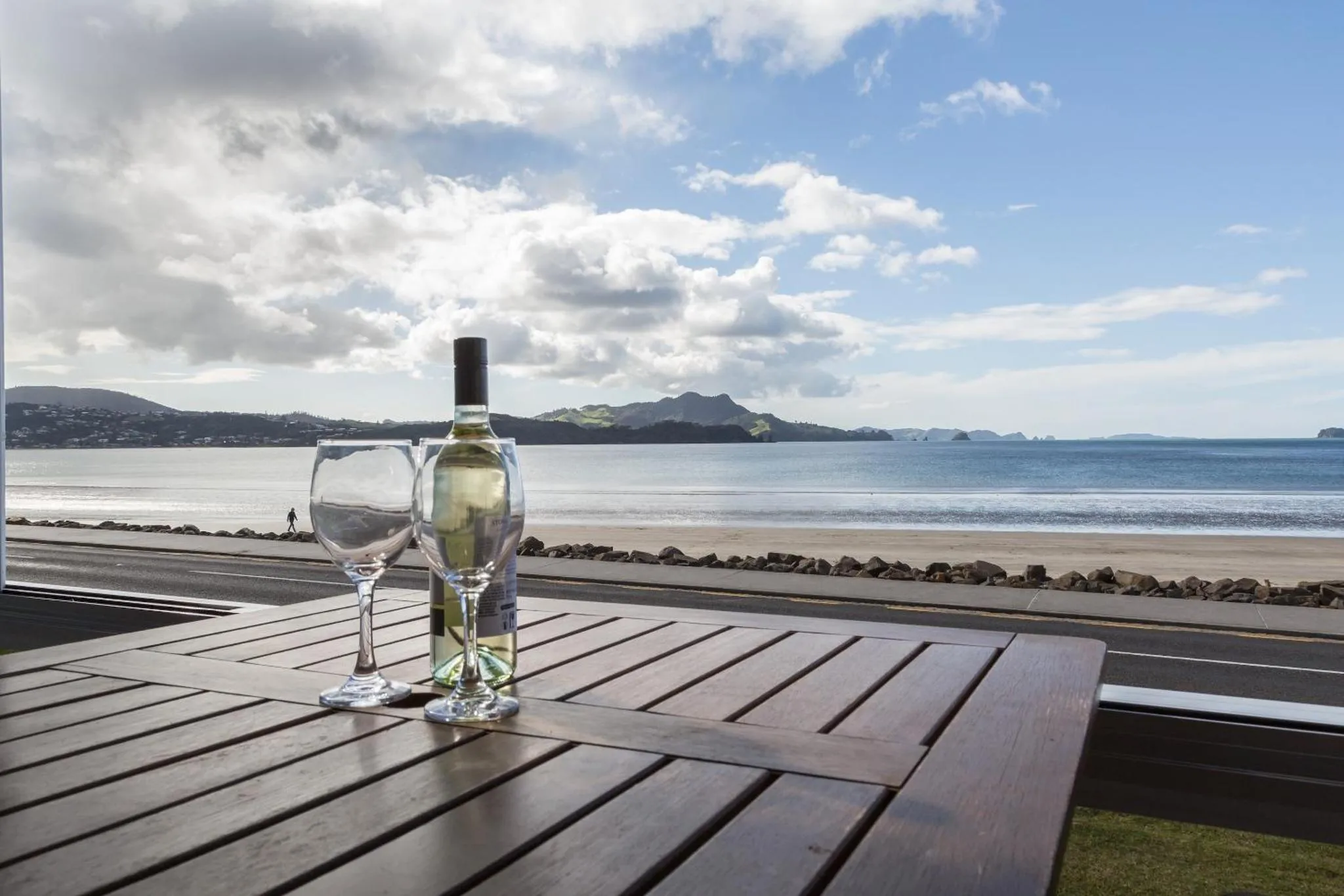 Une bouteille de vin et deux verres sur une table en bois face à la mer.