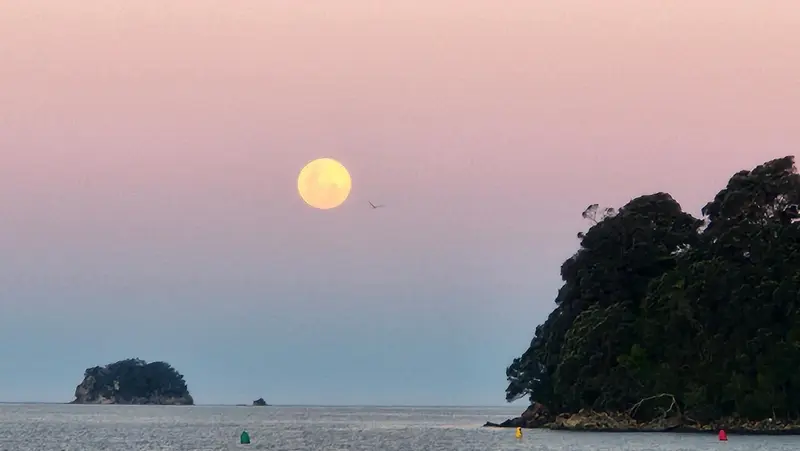 Coucher de soleil sur l'océan avec une pleine lune et des îles au loin.