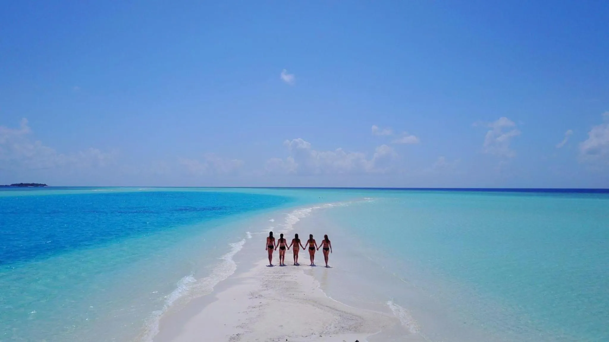 Quatre personnes se tiennent la main sur une étendue de sable blanc au milieu d'une eau turquoise.