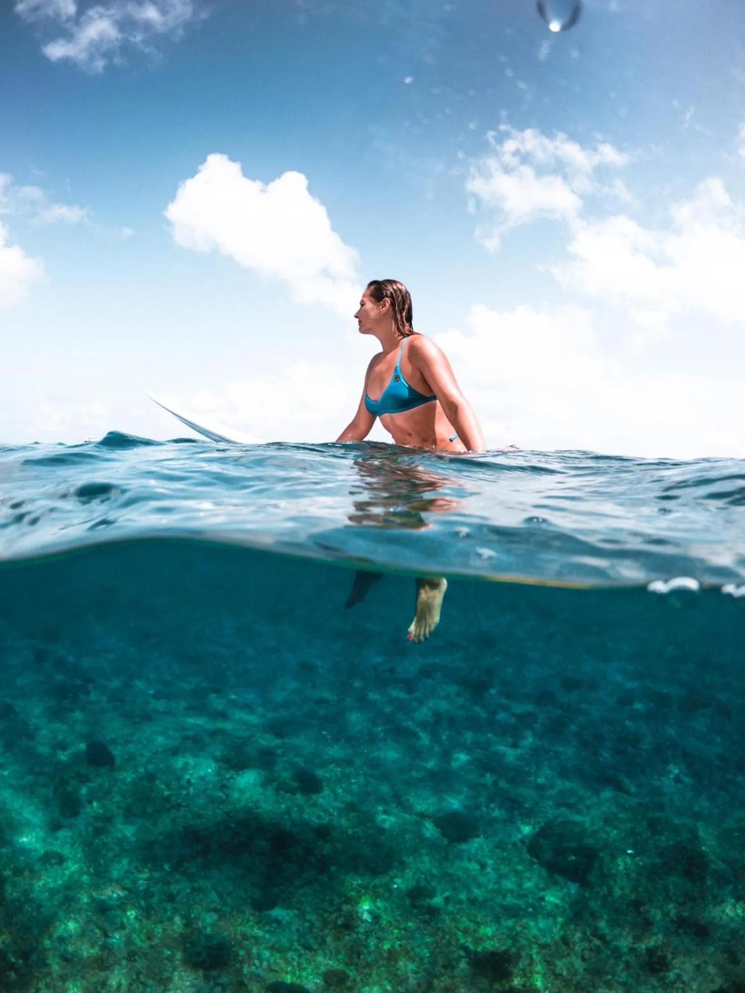 Une femme flotte à la surface de l'eau turquoise, le regard tourné vers l'horizon.