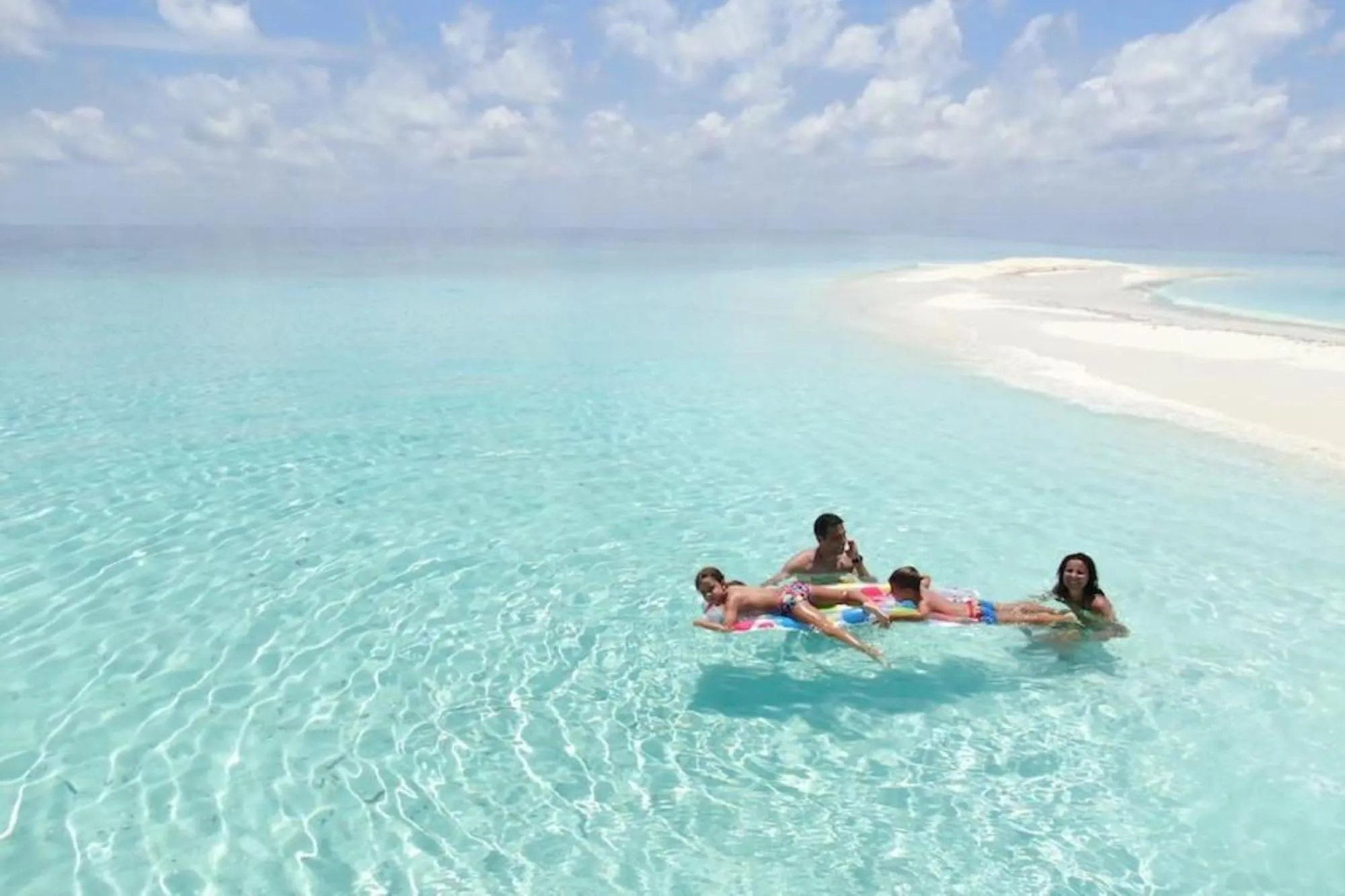Personnes flottant sur des bouées dans une eau turquoise peu profonde.