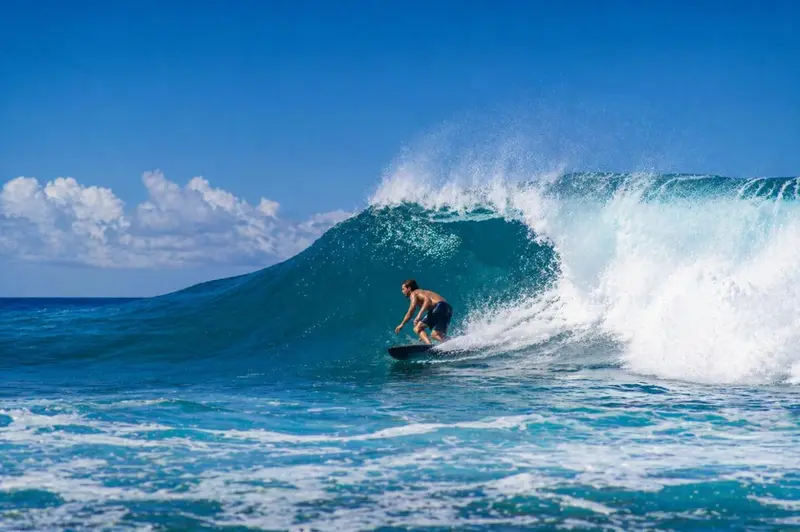 Un surfeur chevauche une vague turquoise sous un ciel bleu.