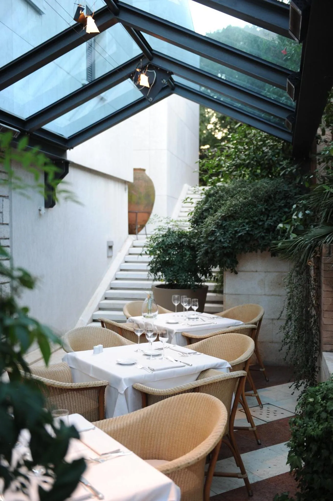 Une table est dressée sur une terrasse ombragée par une verrière.