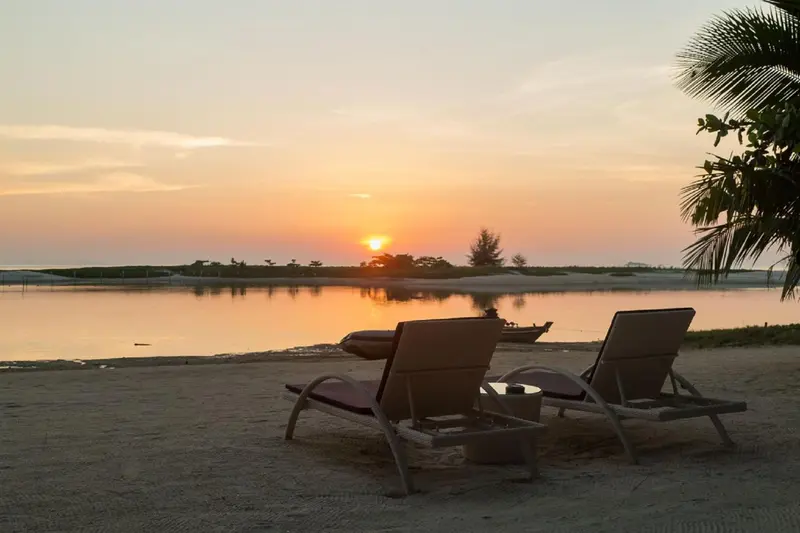 Deux fauteuils de plage invitent à la détente face à un coucher de soleil sur l'océan.