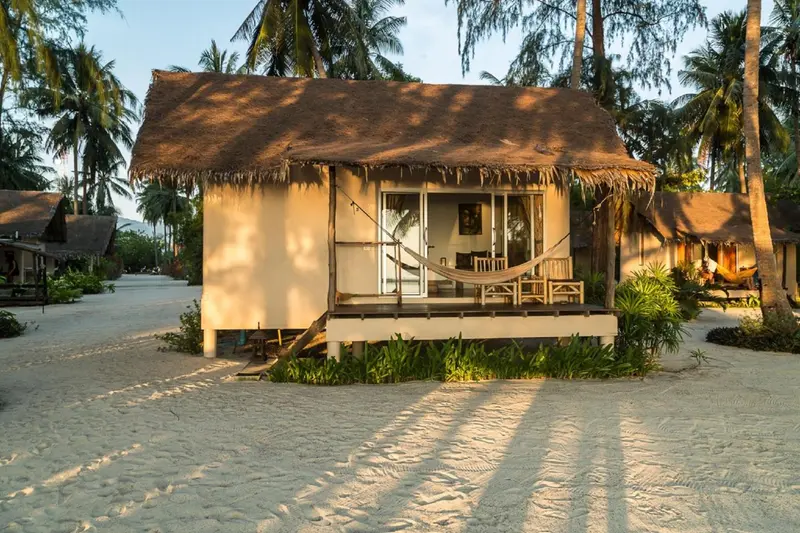 Une cabane de plage en bois avec une terrasse et un hamac.