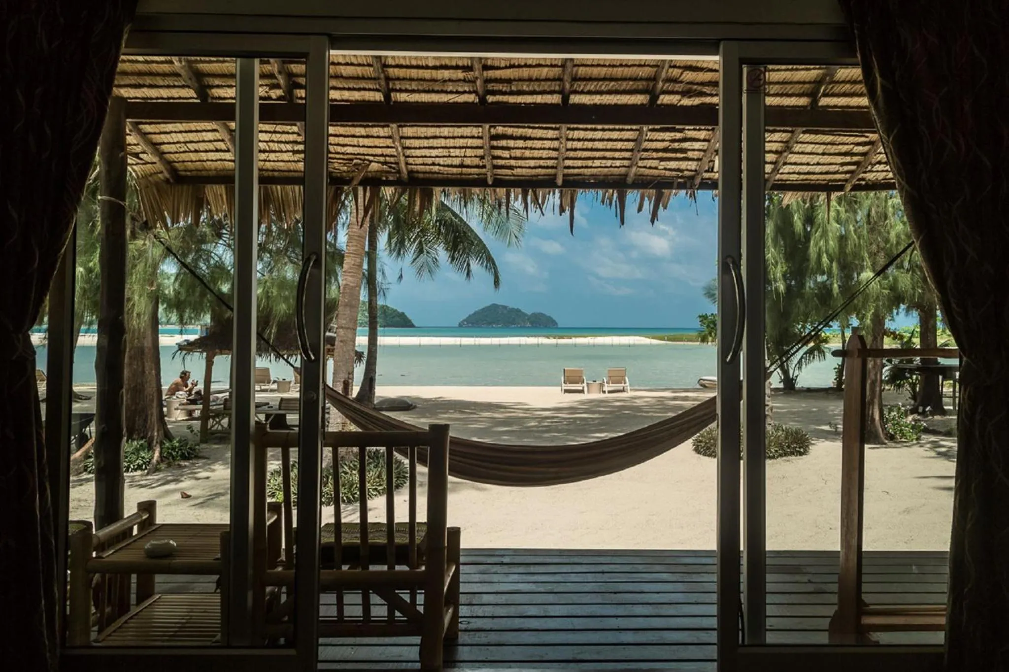 Vue sur une plage de sable blanc et une mer turquoise depuis une terrasse ombragée.