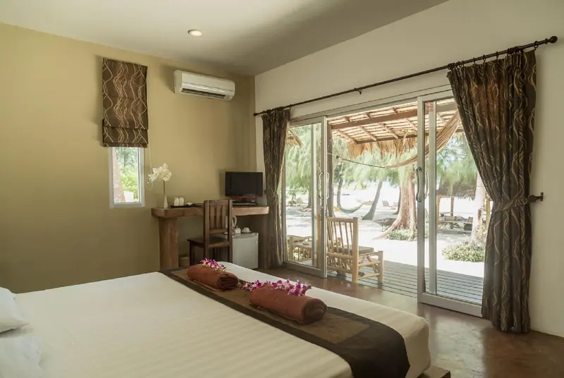 Une chambre lumineuse s'ouvre sur une terrasse en bois avec vue sur la plage.