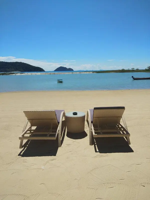 Deux transats et une petite table basse sur une plage de sable fin face à la mer.