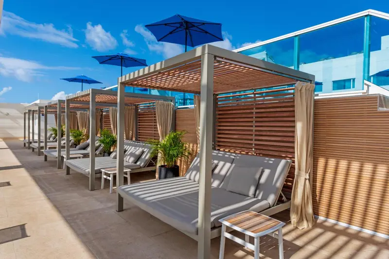 Transats et parasols sous une pergola en bois sur une terrasse ensoleillée.