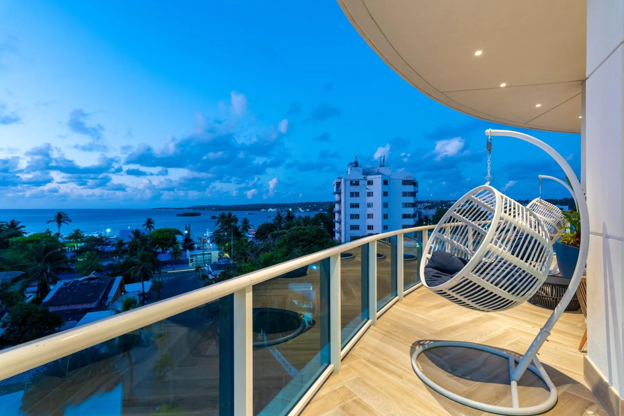 Vue d'un balcon avec un fauteuil suspendu et une vue sur la mer au crépuscule.