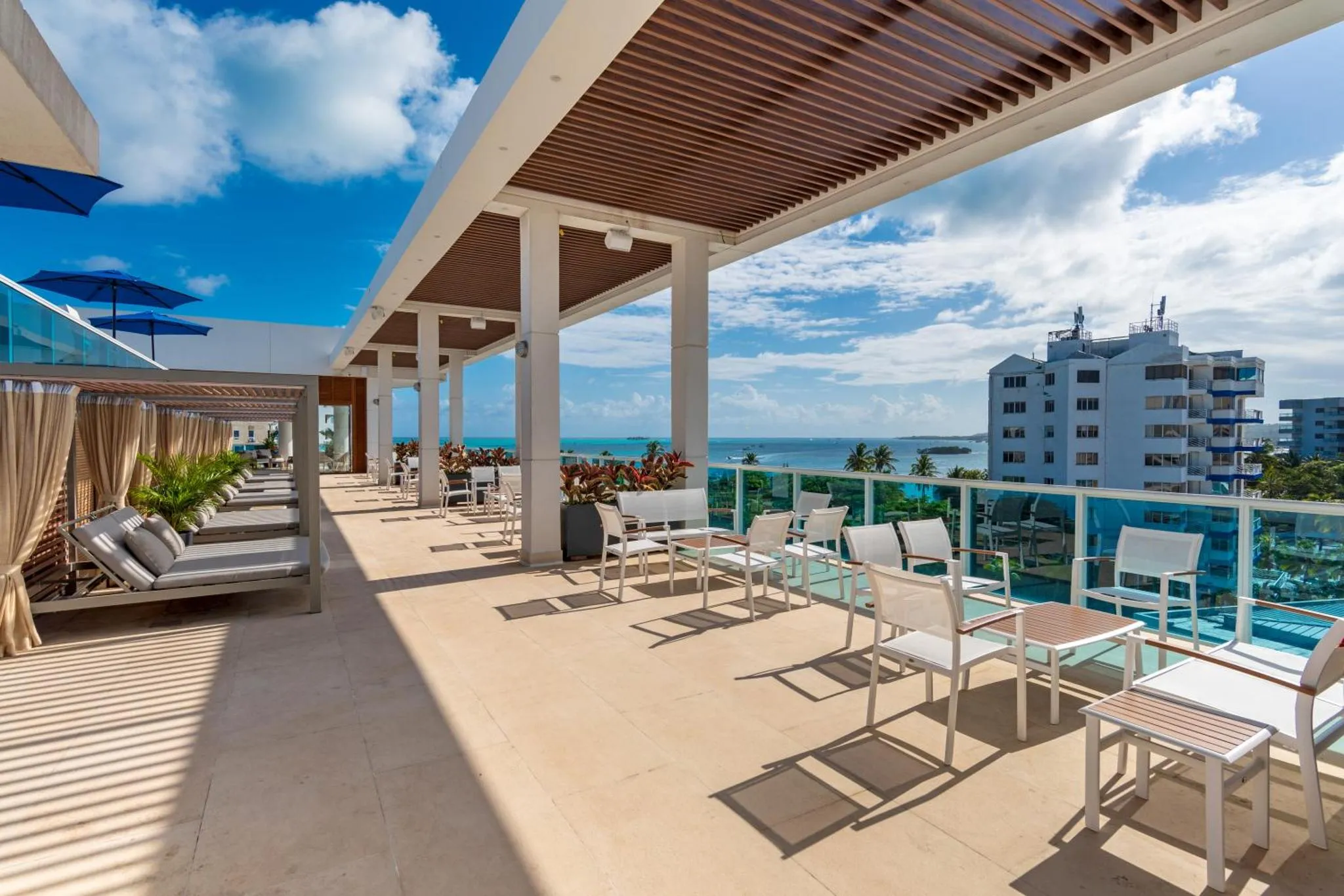 Terrasse aménagée avec transats et tables offrant une vue sur la mer et la ville.