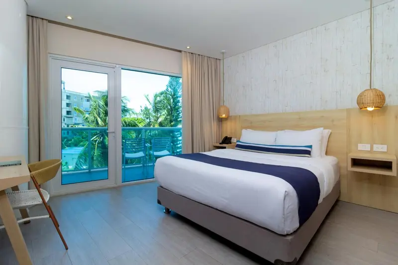 Une chambre lumineuse avec un grand lit et un balcon donnant sur la végétation.