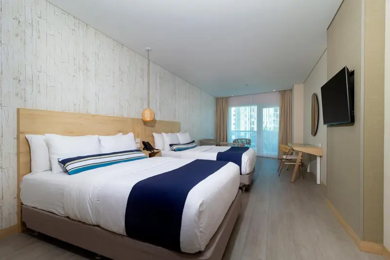 Une chambre lumineuse avec deux lits et un bureau près d'une fenêtre.