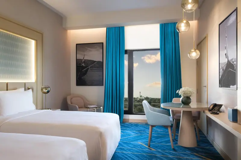 Chambre lumineuse avec un lit blanc et un coin repas près d'une fenêtre.
