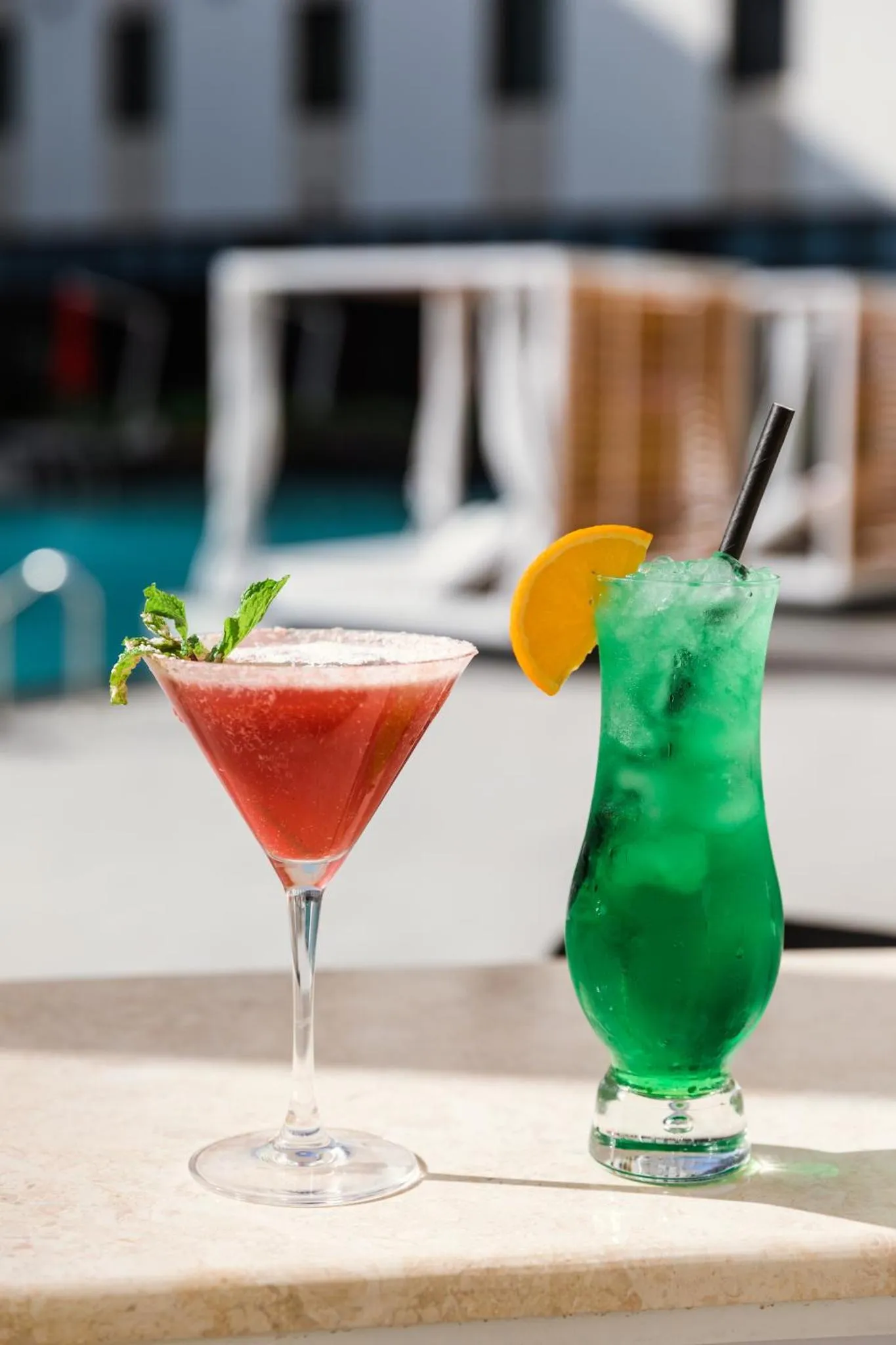 Deux cocktails colorés reposent sur une table près d'une piscine.