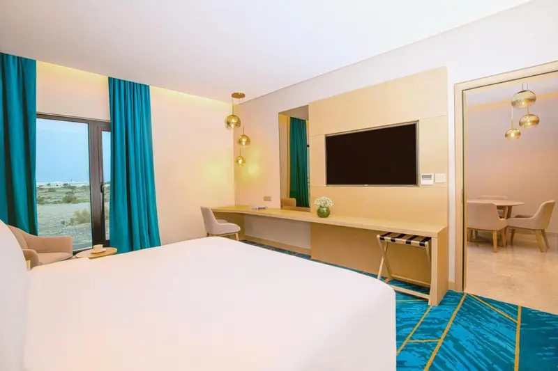 Chambre lumineuse avec un lit blanc et un bureau près d'une fenêtre.